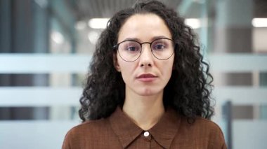 Modern cam ofiste bir iş yerinde duran ciddi bir iş kadınının portresi. Gözlüklü, kendine güvenen iş kadınının kameraya bakışının vesikalığı. Çalışma alanında başarılı bir bayan yönetici. Kapat.