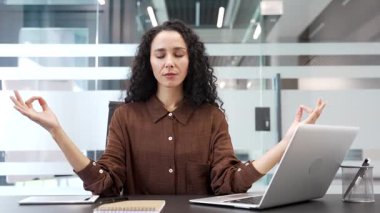 Odaklanmış iş kadını, ofisteki bir iş yerinde otururken gözleri kapalı meditasyon yapıyor. Genç bir kadın yoga yapıyor, huzuru hissediyor. Kadın çalışan stresten kurtulmak için işe ara verdi.