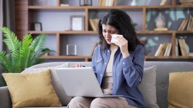 Üzgün genç bir kadın evdeki oturma odasında kanepede otururken dizüstü bilgisayar kullanan bir psikologla görüntülü konuşma yapıyor. Duygusal kadınlar online danışma sırasında ağlarlar, sorunlarını anlatırlar.