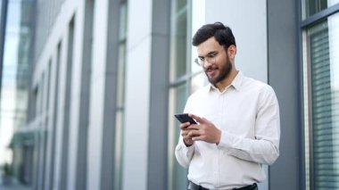 Bir iş adamı modern bir ofis binasının yanında caddede dururken bir cep telefonu kullanır. İnternette sohbet eden yakışıklı bir erkek, internette geziniyor ya da akıllı telefondan mesaj yazıyor.