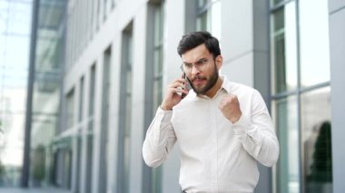 Kızgın hoşnutsuz işadamı iş yeri binasının yakınında telefonda konuşurken tartışıyor. Heyecanlı adam duygularını ifade ediyor, stresli iş durumlarıyla uğraşıyor, çatışma çözülüyor.