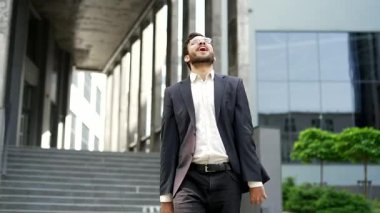 Mutlu iş adamı ofis binasının yakınındaki sokakta yürürken başarısını kutluyor. Resmi takım elbiseli neşeli, pozitif girişimci bir zafer jesti sergilediği için sevinçlidir.