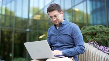 Kendine güvenen iş adamı, iş yerinin yanındaki bankta oturan dizüstü bilgisayarda çalışıyor. Yakışıklı bir adam internette ya da internette sohbet ediyor. Freelancer müşterisiyle uzaktan iletişim kurar. Kapat.