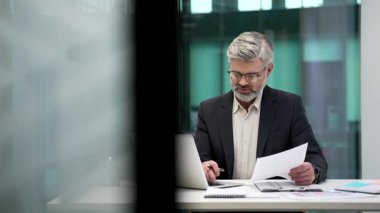 Resmi takım elbiseli bir yetişkin finansör iş yerinde çalışırken dizüstü bilgisayarla evrak işleriyle uğraşıyor. Odaklanmış işadamı mali raporla ilgileniyor, muhasebe ile ilgileniyor.