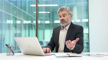 Hüsrana uğramış yetişkin iş adamı, modern iş ofisindeki iş yerinde dizüstü bilgisayarını kullanarak işlem yapmakta zorlanıyor. Kafası karışmış erkek işçi bilgisayarda çalışırken sorunlar yaşıyor