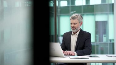 İş yerindeki bir dizüstü bilgisayarda çalışan kendinden emin bir iş adamı. Resmi takım elbiseli bir girişimci bilgisayarda yazı yazıyor, internette sohbet ediyor ya da iş yerinde projeyle meşgul.