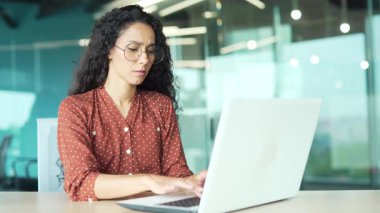 İş yerinde çalışırken dizüstü bilgisayarla çalışırken baş ağrısı çeken bitkin genç bir iş kadını. Yorgun kadın acı hissediyor, alnına ve şakaklarına eliyle masaj yapıyor.