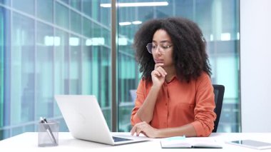 Düşünceli genç Afrikalı Amerikalı iş kadını ofisteki bilgisayarında daktilo yazmayı düşünüyor. Ciddi siyahi kadın çalışanlar, görevleriyle meşgul olarak proje üzerinde çalışıyorlar.