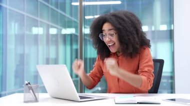Mutlu Afro-Amerikan iş kadını laptopta harika haberler okuyor modern iş ofisindeki masasında oturuyor. Neşeli siyah kadın başarıyı kutluyor, zaferi kutluyor.