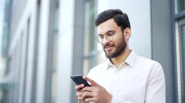 Bir iş adamı modern bir ofis binasının yanında caddede dururken bir cep telefonu kullanır. Yakışıklı erkek işçi internette sohbet ediyor, internette geziniyor ya da akıllı telefondan mesajlar yazıyor. Kapat.