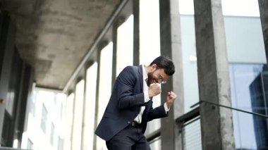 Mutlu iş adamı ofis binasının merdivenlerinden inişini kutluyor. Resmi takım elbiseli neşeli, pozitif girişimci bir zafer jesti sergilediği için sevinçlidir.