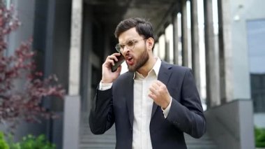 Resmi takım elbiseli kızgın bir işadamı telefonda konuşuyor. Ofis binasının yanında duruyor. Sinirli bir patron astlarını azarlar ve bağırır, stresli iş durumları, çatışma çözümleri