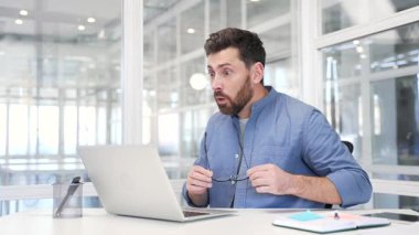 İnanılmaz mutlu iş adamı dizüstü bilgisayara ve iş yerindeki iş yerinde oturan kameraya şaşırdı. Heyecanlı adam kadehleri vurdu, hoş içerikler gördü, harika haberler başarıyı kutladı.