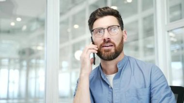 Modern ofisteki işyerinde otururken kendine güvenen bir işadamı cep telefonuyla konuşuyor. Yönetici bir müşteriyle iletişim kurar ya da iş ortağıyla akıllı telefon kullanarak iletişim kurar. Kapat.