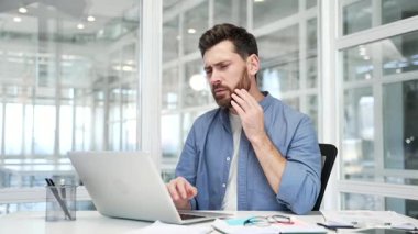 İş yerindeki çalışma masasında dizüstü bilgisayarla çalışırken diş ağrısı çeken üzgün bir işadamı. Erkek işçi, elini yanağında tutuyor ve masaj yapıyor. Bir dişçiye görünmesi gerekiyor.