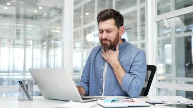 Modern bir iş yerinde dizüstü bilgisayarla çalışırken boğazı ağrıyan hasta işadamı. Erkek işçi soğuk algınlığı, virüs ya da grip olmuş. Üzgün bir adam elinde yaralı bir spo tutuyor.