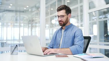 Tatmin olmuş mutlu iş adamı, modern iş ofisindeki bir masada otururken dizüstü bilgisayarından harika haberler aldı. Gülümseyen yakışıklı girişimci bilgisayardan olumlu bir mesaj okuyor.