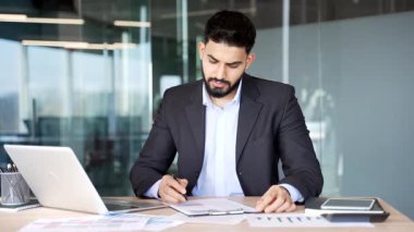 Resmi takım elbiseli bir işadamı iş yerindeki bir masada oturan belgeleri imzalıyor. Kendine güveni olan bir patron evraklarla dosyaya bakar, kontrol eder ve sözleşmeyi kalemle imzalar.