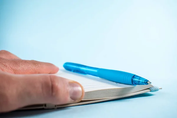 Mavi arka plandaki bir defterde el ve mavi kalem