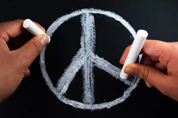 stock image Hands drawing peace symbol with white chalks on blackboard