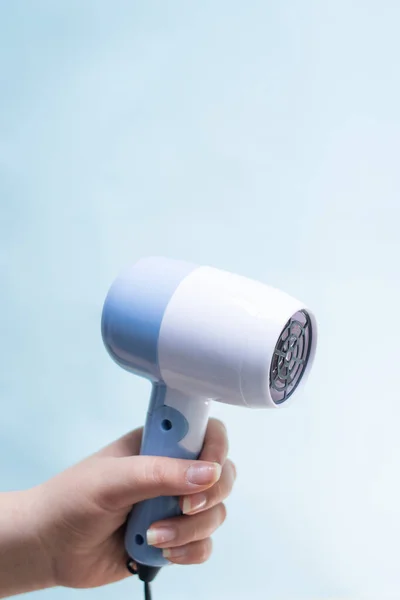 Hand holding a blue hair dryer on blue background