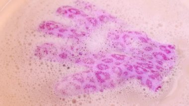 Pembe arka planda sabun ve köpükle banyo eldiveni.