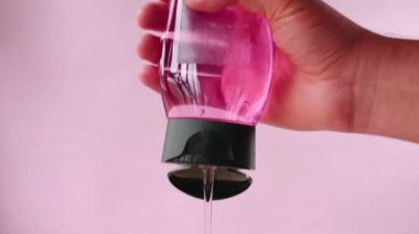 Pembe arka planda pembe bir şampuan şişesi tutuyor.