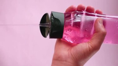 Pembe arka planda pembe bir şampuan şişesi tutan el videosu.