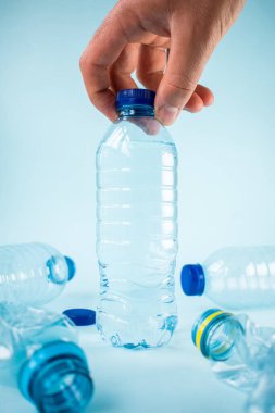 Mavi arka planda su şişesi alan el.