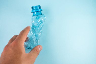 Mavi arka planda plastik şişeyi alan el.