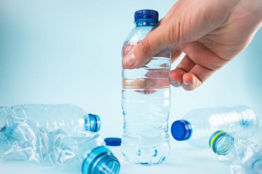 Mavi arka planda su şişesi alan el.