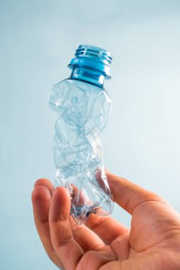 Mavi arka planda plastikten yapılmış şişeyi tutan el.