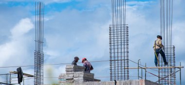 Adam inşaatta çalışıyor ve kask ve koşum takımı kullanıyor.