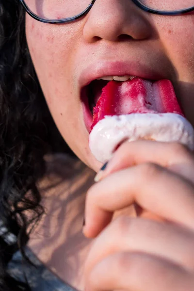 Güneşli bir günde kırmızı donmuş böğürtlenli dondurmayı ısıran diş teli takan bir kız.