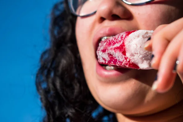 Güneşli bir günde kırmızı donmuş böğürtlenli dondurmayı ısıran diş teli takan bir kız.