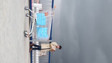 Vertical video of market car and man looking his phone in a parking on cloudy day