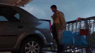Man getting bags in a car trunk from a metal market car in a parking lot