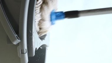 Vertical video of man squeezing a mop on a plastic mop squeezer on blue background