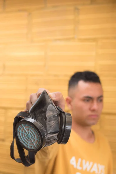 Sarı arka planda gaz maskesi tutan adam.