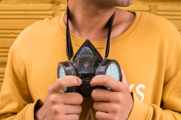 Adam sarı arka planda gaz maskesini çıkarıyor.