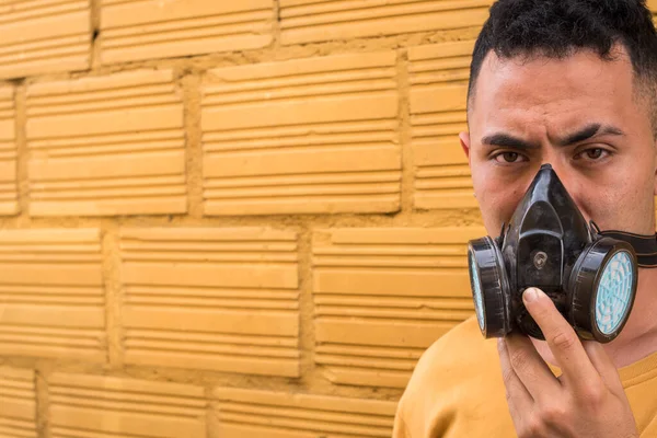 Adam sarı arka planda gaz maskesini çıkarıyor.