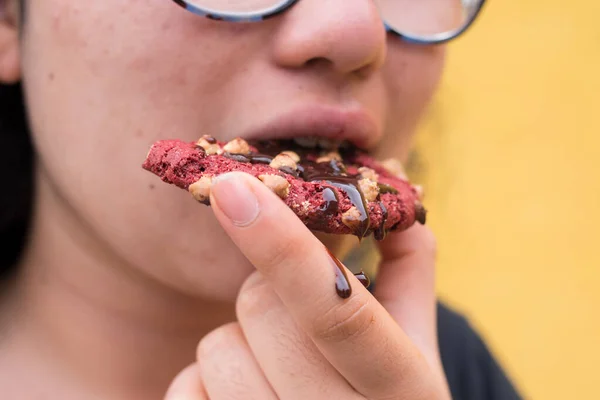 Girl bitting a red chocolate cookies with chocolate sauce