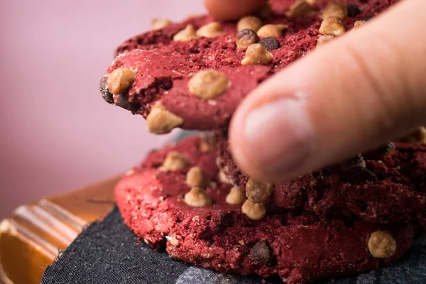 Hand taking red chocolate cookie with chips on wooden table