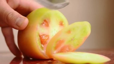 Adam yeşil domates dilimlerini metal bir bıçakla kesiyor.