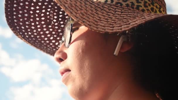 Γυναίκα Που Φοράει Ψάθινο Καπέλο Και Βγάζει Ακουστικό Την Ηλιόλουστη — Αρχείο Βίντεο