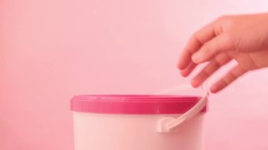 Eller pembe arka planda pembe kapaklı beyaz kovayı açıyor