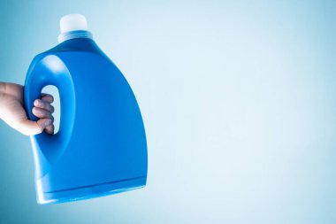 Mavi arka planda mavi sıvı sabun şişesini tutan el.