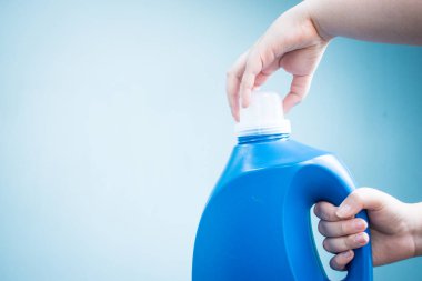 Mavi arka planda mavi sıvı sabun şişesini tutan el.