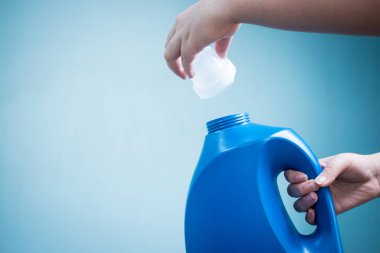 Mavi arka planda mavi sıvı sabun şişesini tutan el.