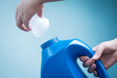 Mavi arka planda mavi sıvı sabun şişesini tutan el.